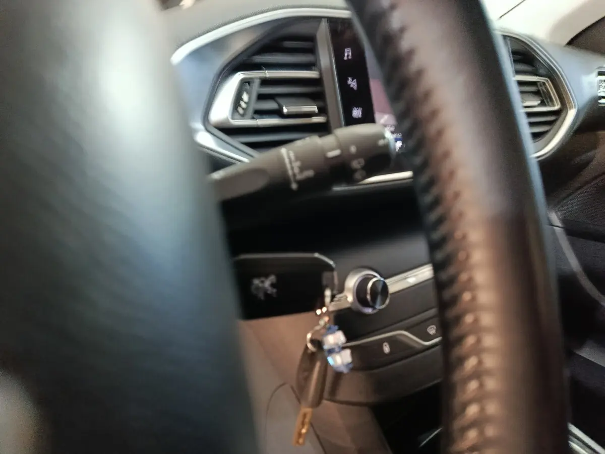 Intérieur de la Peugeot 308 2021 vu à travers le volant cuir, avec clé insérée et commandes du tableau de bord visibles.