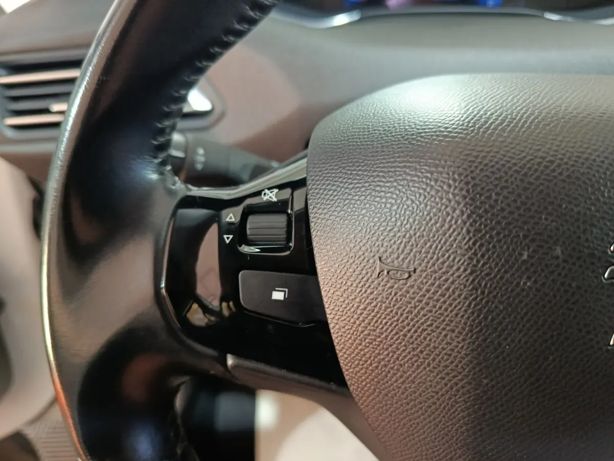 Gros plan sur la partie gauche du volant cuir de la Peugeot 308 blanc, avec commandes intégrées au volant.