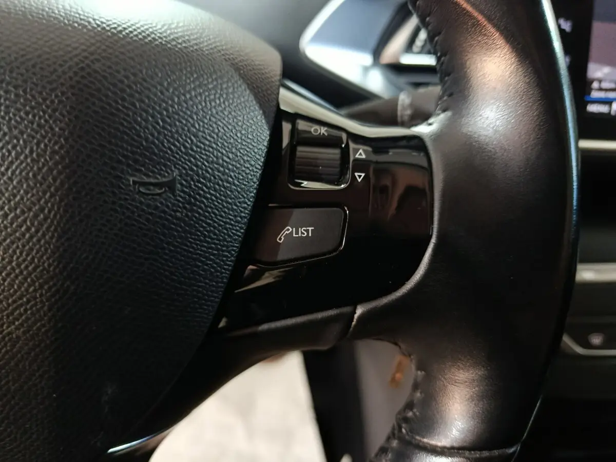 Gros plan sur le volant cuir noir de la Peugeot 308 BlueHDi 130, avec commandes vocales et boutons multifonctions visibles.