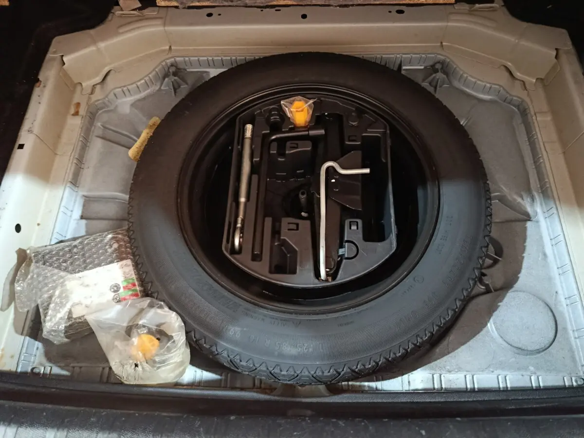 Vue de dessus du coffre ouvert d'une Peugeot 308 blanche, montrant la roue de secours et les outils de bord.