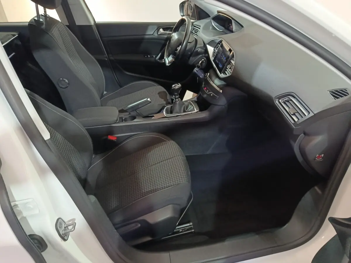 Vue intérieure côté conducteur de la Peugeot 308 blanche 2021, avec tableau de bord moderne et boîte manuelle.