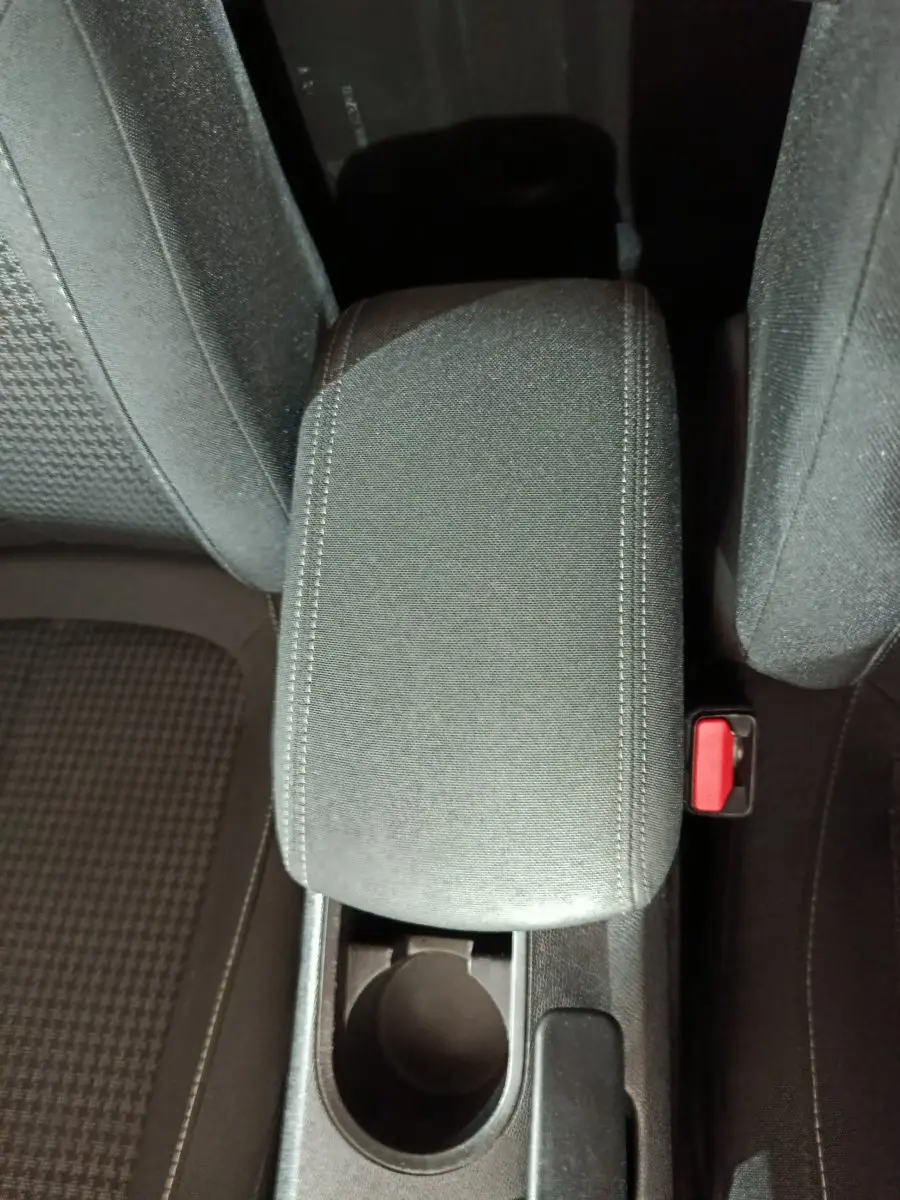 Vue plongeante sur l'accoudoir central noir et porte-gobelet entre les sièges avant de la Peugeot 308 blanche.