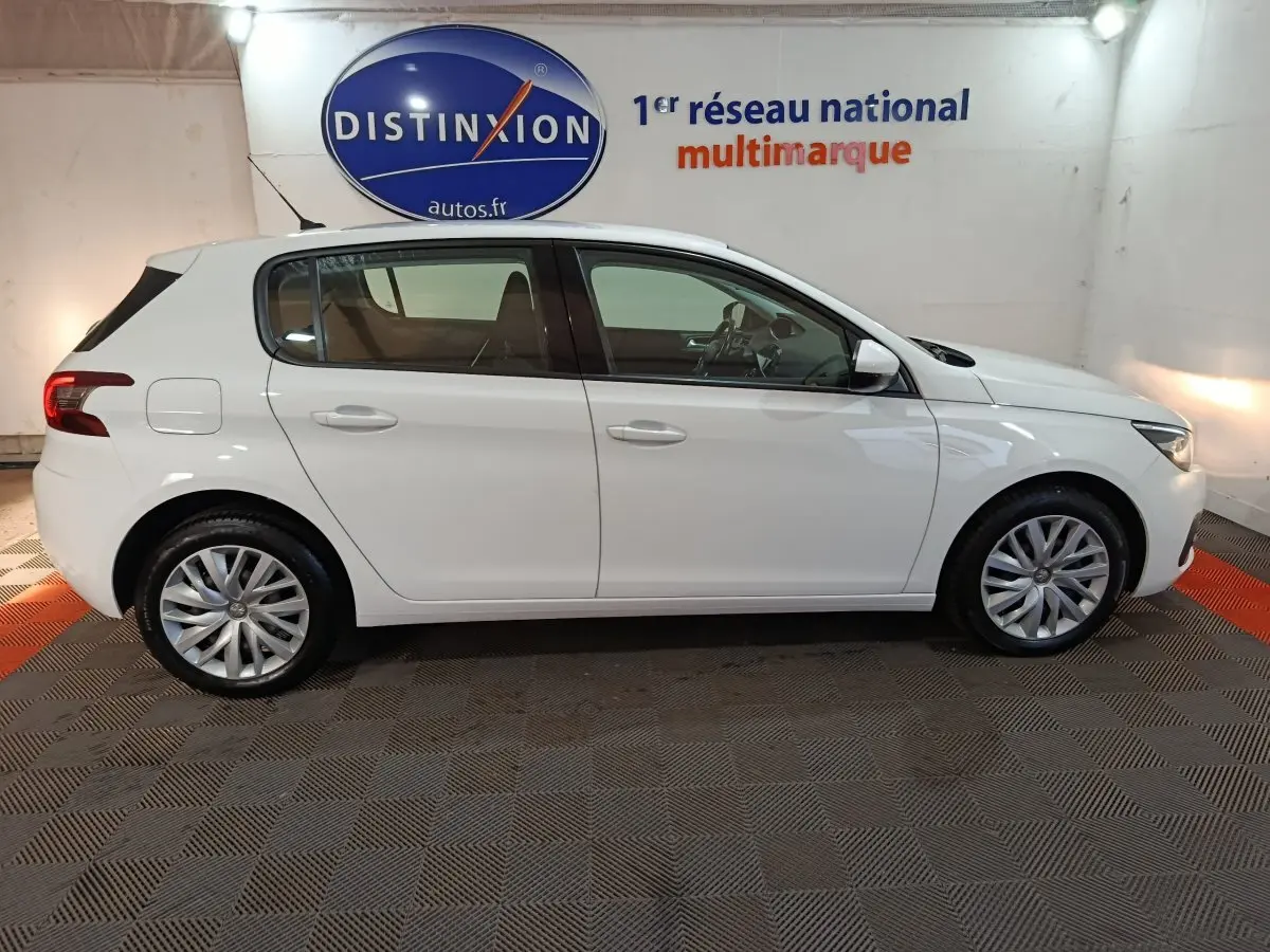 Profil droit d'une Peugeot 308 blanche 2021 dans un showroom avec logo Distinxion en arrière-plan.