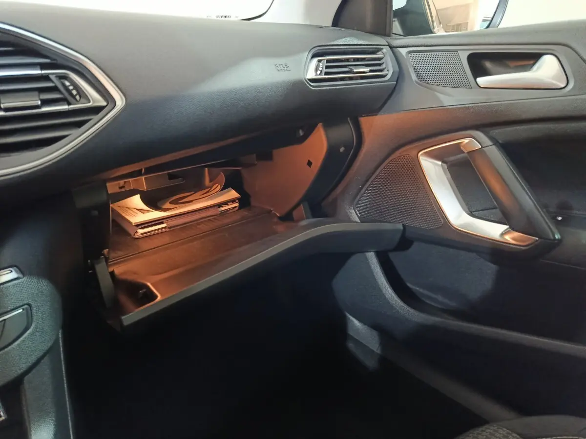 Intérieur noir de la Peugeot 308 2021, vue côté passager avec boîte à gants ouverte et poignée argentée.