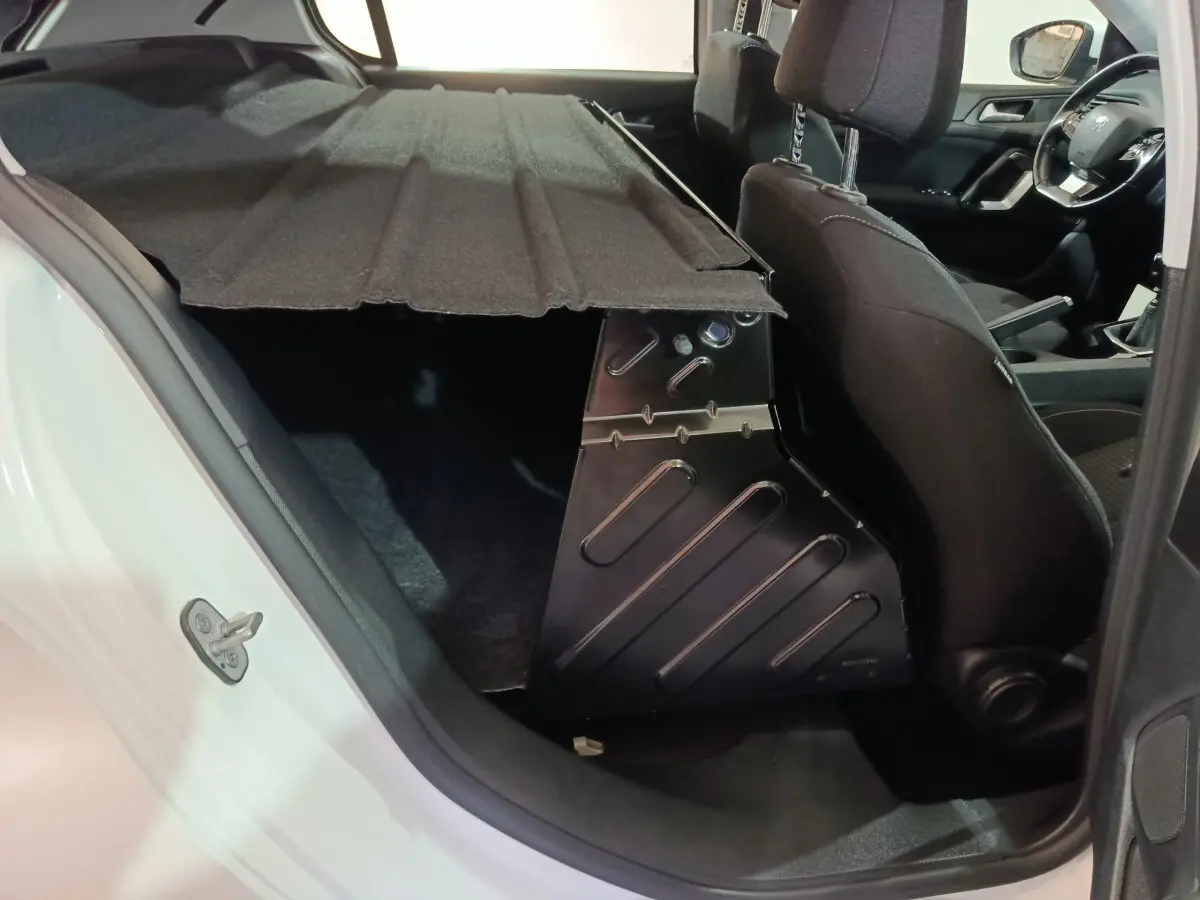 Vue intérieure côté gauche du coffre avec cloison rigide et sièges avant noirs dans une Peugeot 308 blanche 2021