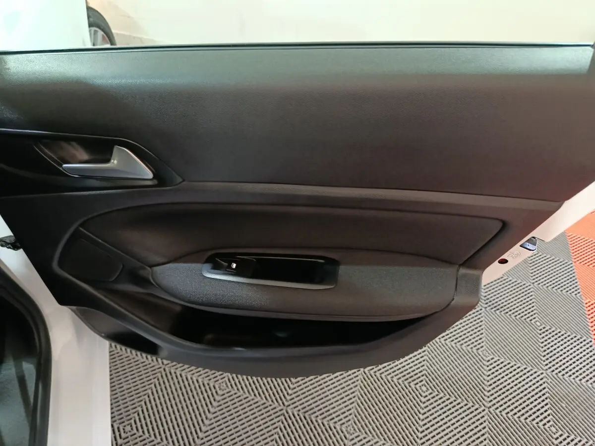 Vue intérieure sur la porte côté gauche d'une Peugeot 308 blanche, avec garniture noire et poignée intégrée.