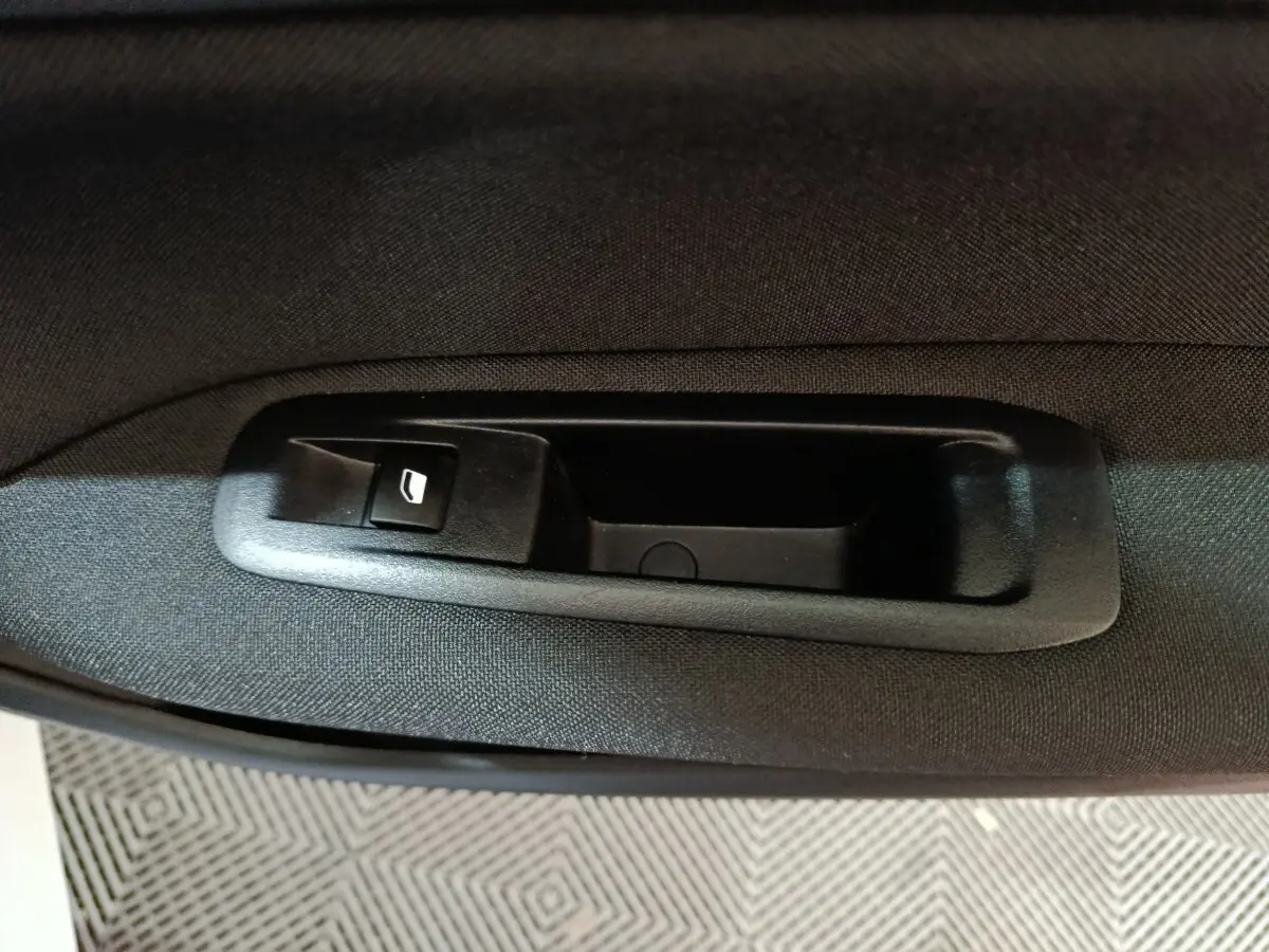 Gros plan sur le bouton de commande de lève-vitre côté conducteur dans l'habitacle noir de la Peugeot 308 blanche.