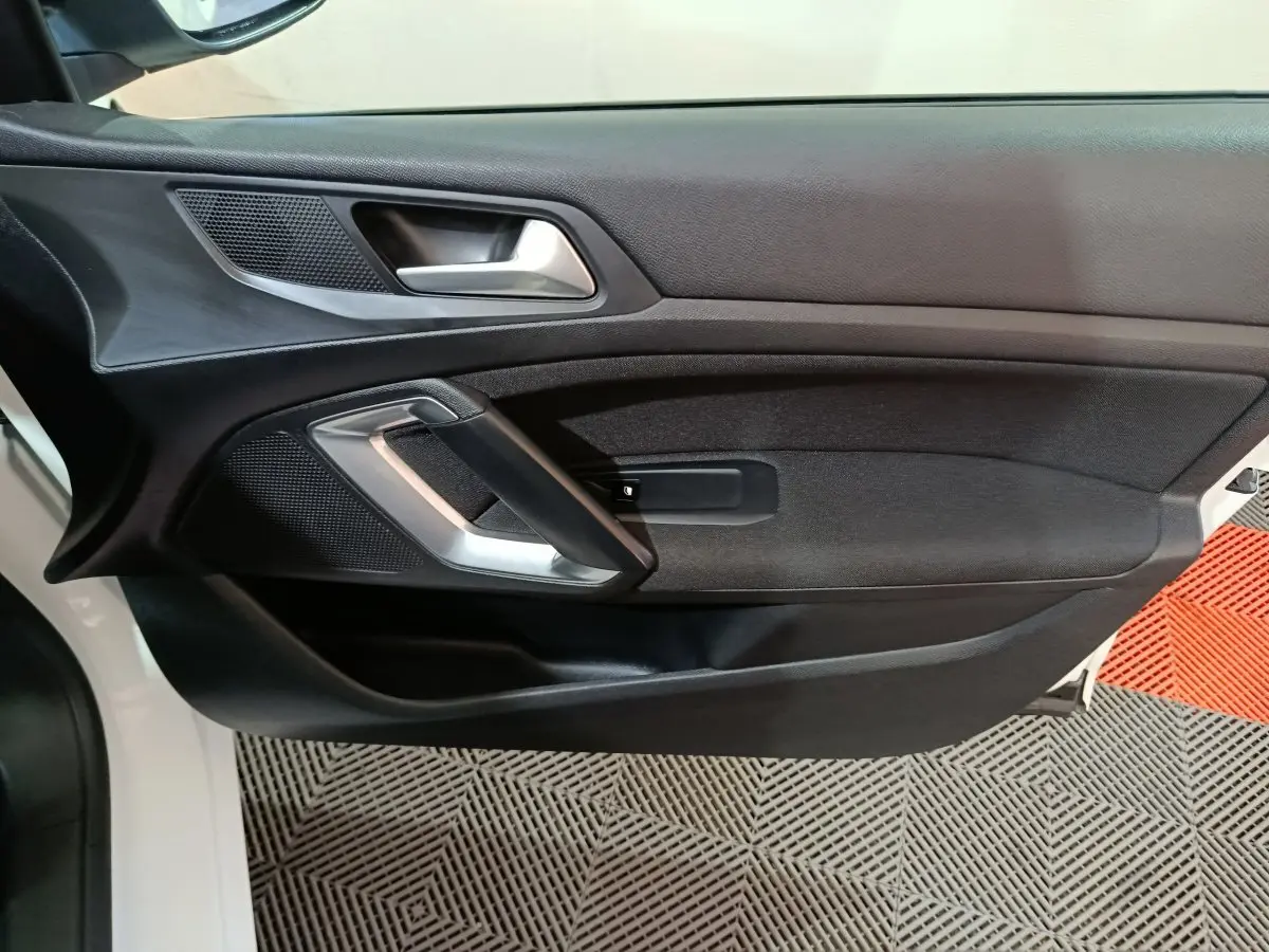 Vue rapprochée de la porte avant gauche noire de la Peugeot 308 blanche, avec poignée argentée et haut-parleur intégré.