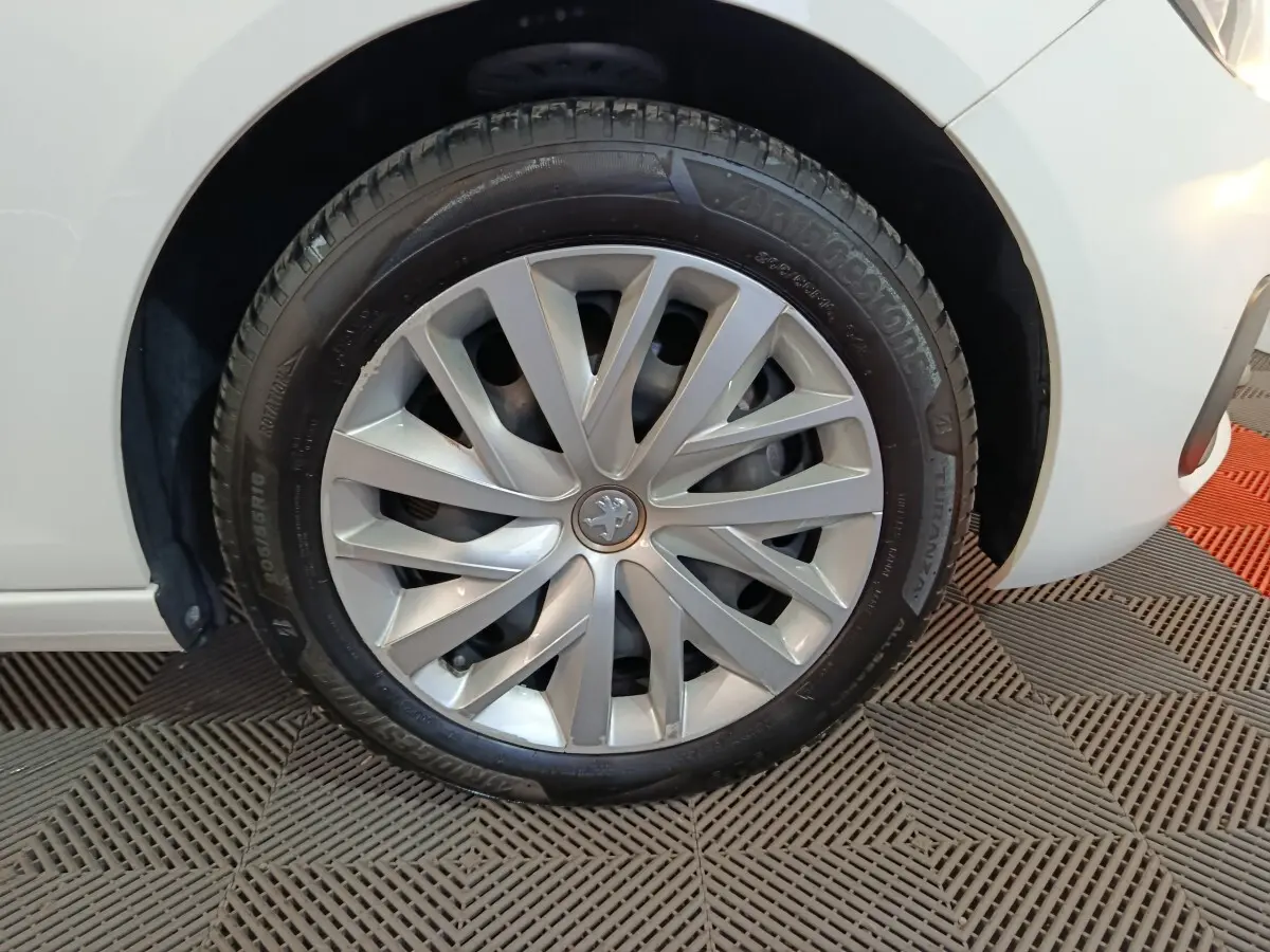 Gros plan sur la roue avant gauche d'une Peugeot 308 blanche, mettant en valeur la jante argentée au design moderne.