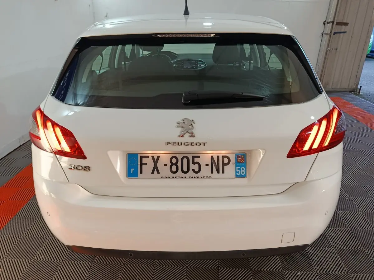 Vue arrière d'une Peugeot 308 blanche avec feux arrière allumés et plaque d'immatriculation française visible