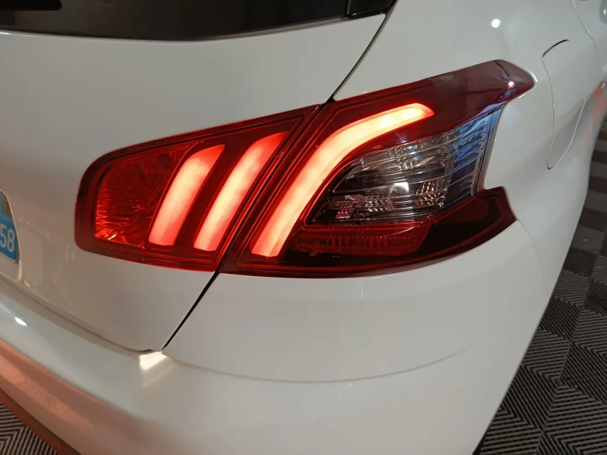 Feu arrière droit allumé sur Peugeot 308 blanc, vue rapprochée du coin arrière du véhicule.