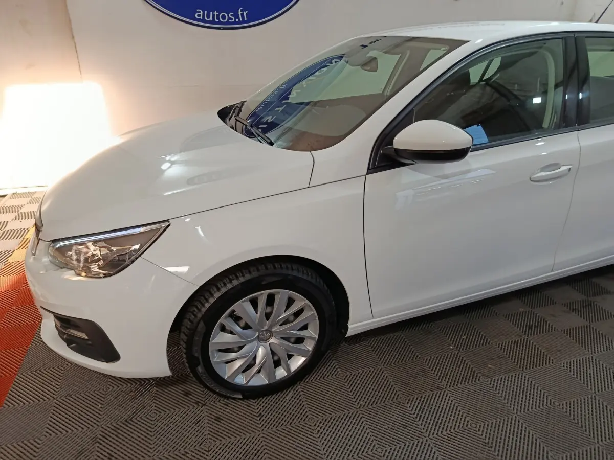 Vue 3/4 avant côté gauche d'une Peugeot 308 blanche avec phares ellipsoïdaux et jantes alliage visibles