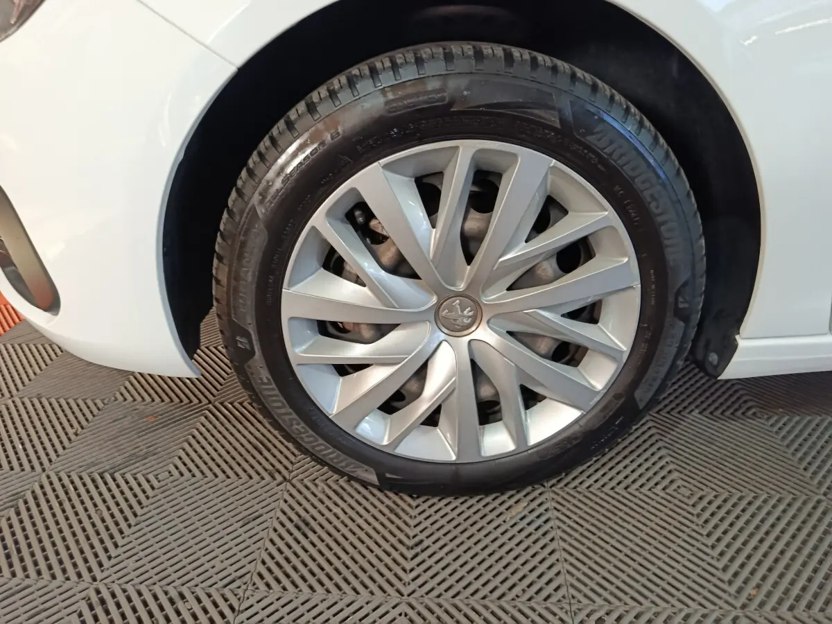 Gros plan sur la roue avant gauche d'une Peugeot 308 blanche, mettant en valeur la jante argentée et le logo lion central.