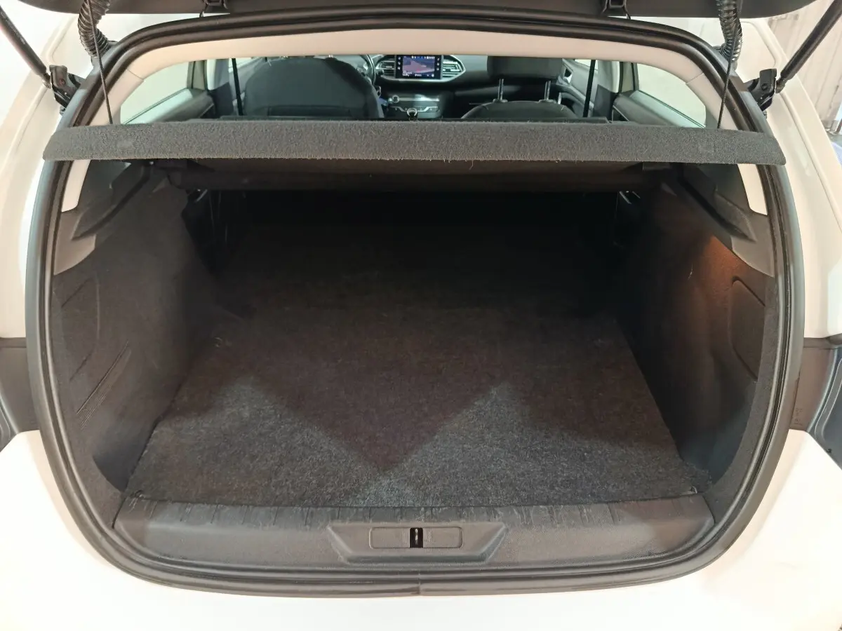 Coffre ouvert vue arrière d'une Peugeot 308 blanche, montrant un espace de chargement propre et spacieux.