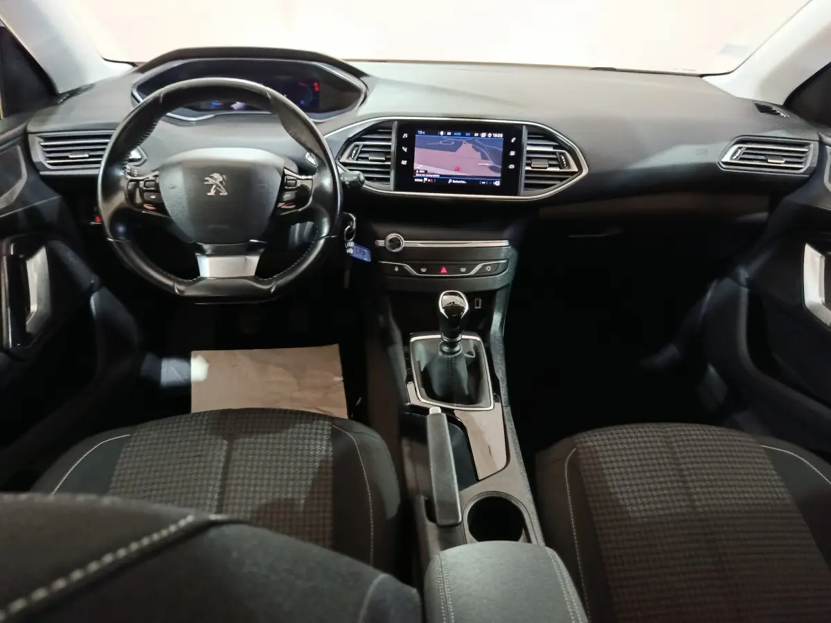 Vue intérieure frontale du poste de conduite de la Peugeot 308 blanche, avec volant cuir et écran tactile central allumé.