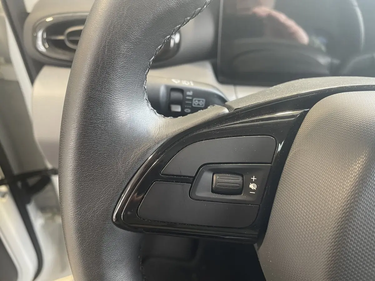 Gros plan sur le volant cuir multifonctions côté gauche du LEAPMOTOR T03 Luxury blanc, avec commandes intégrées.