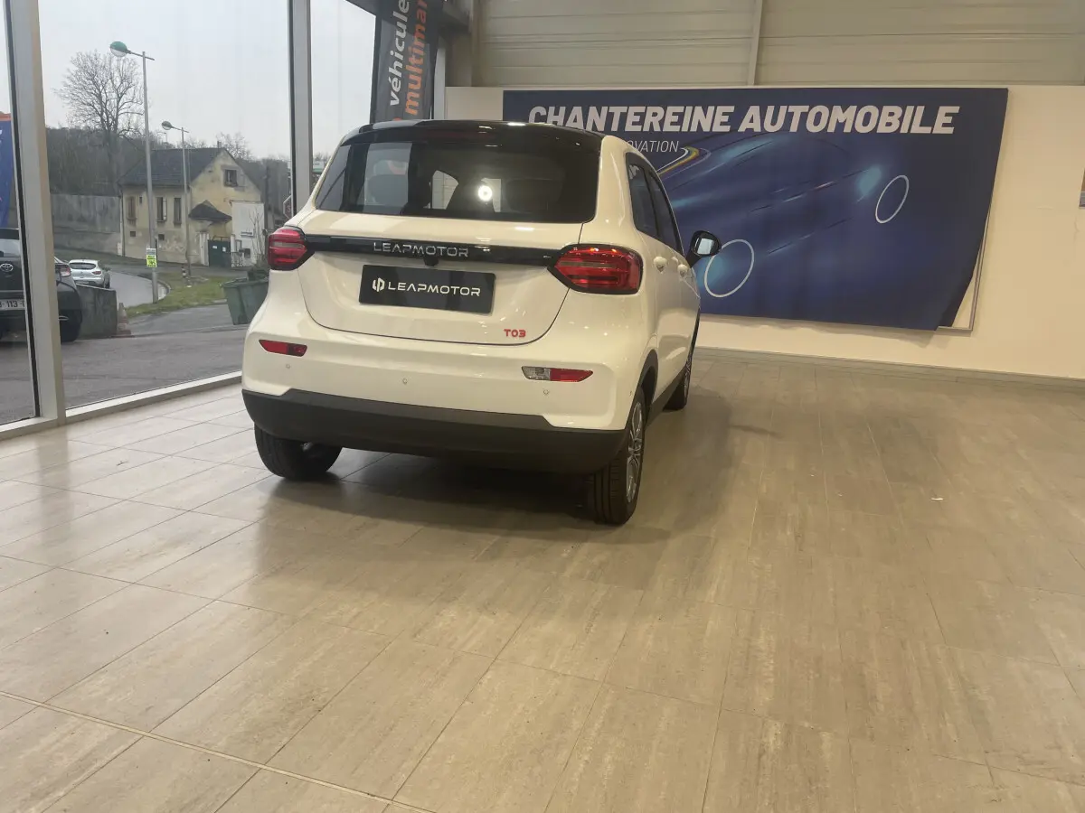 Vue 3/4 arrière d'une LEAPMOTOR T03 blanche dans un showroom avec logo visible sur le mur.