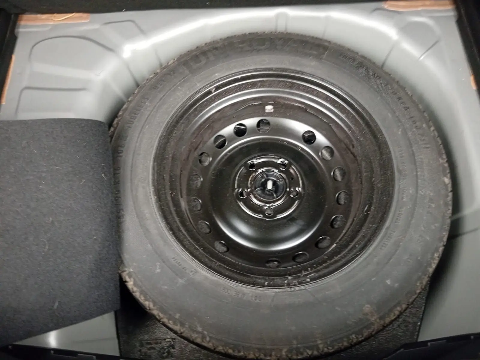 Pneu de secours noir monté dans le coffre d'un Renault Captur 1.3 Mild Hybrid 140 Techno gris cassiopée.