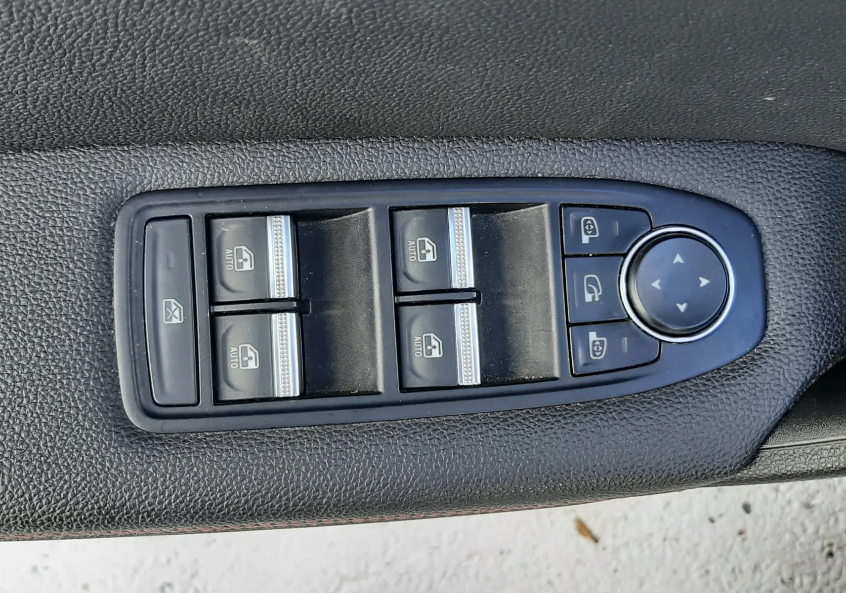 Gros plan sur les commandes des vitres électriques et rétroviseurs sur la porte côté conducteur d'un Renault Captur blanc toit noir.