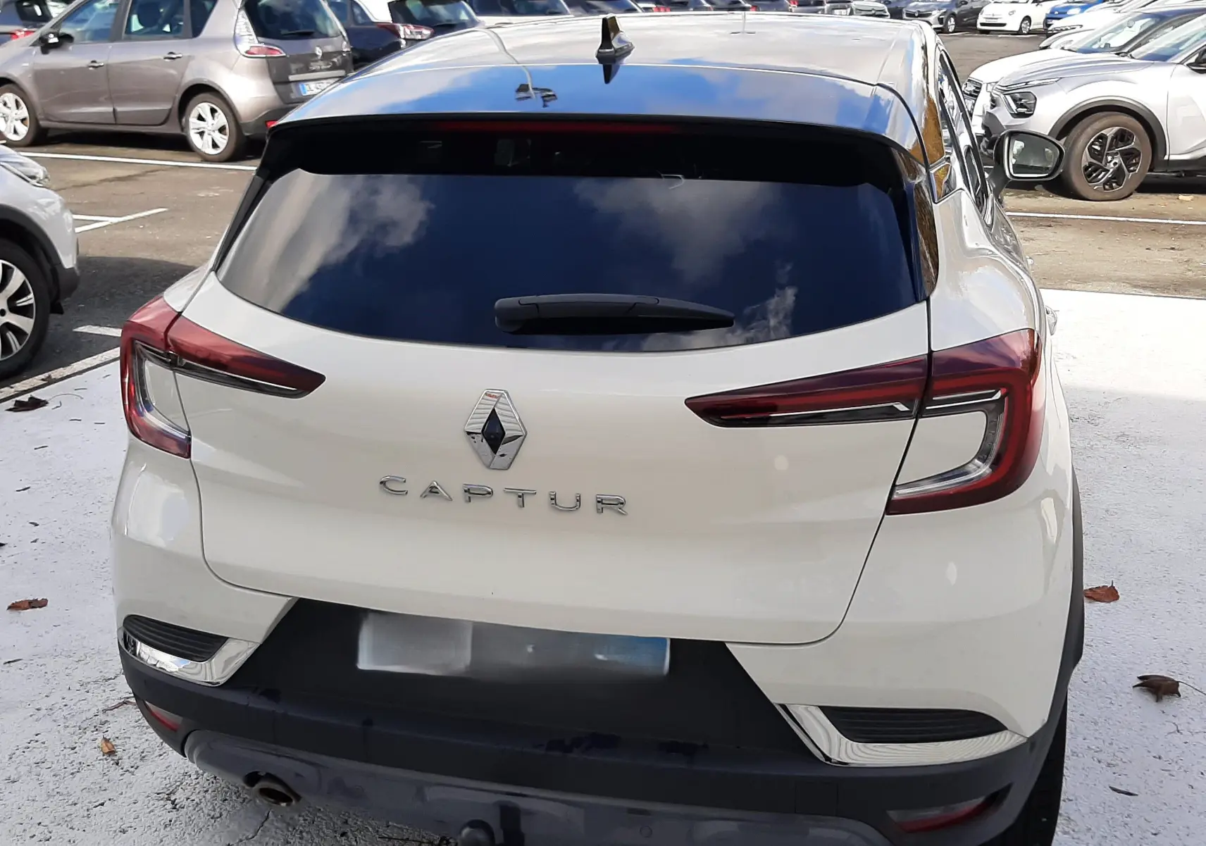 Vue arrière d'un Renault Captur blanc avec toit noir, mettant en valeur ses feux arrière étirés et sa lunette teintée.
