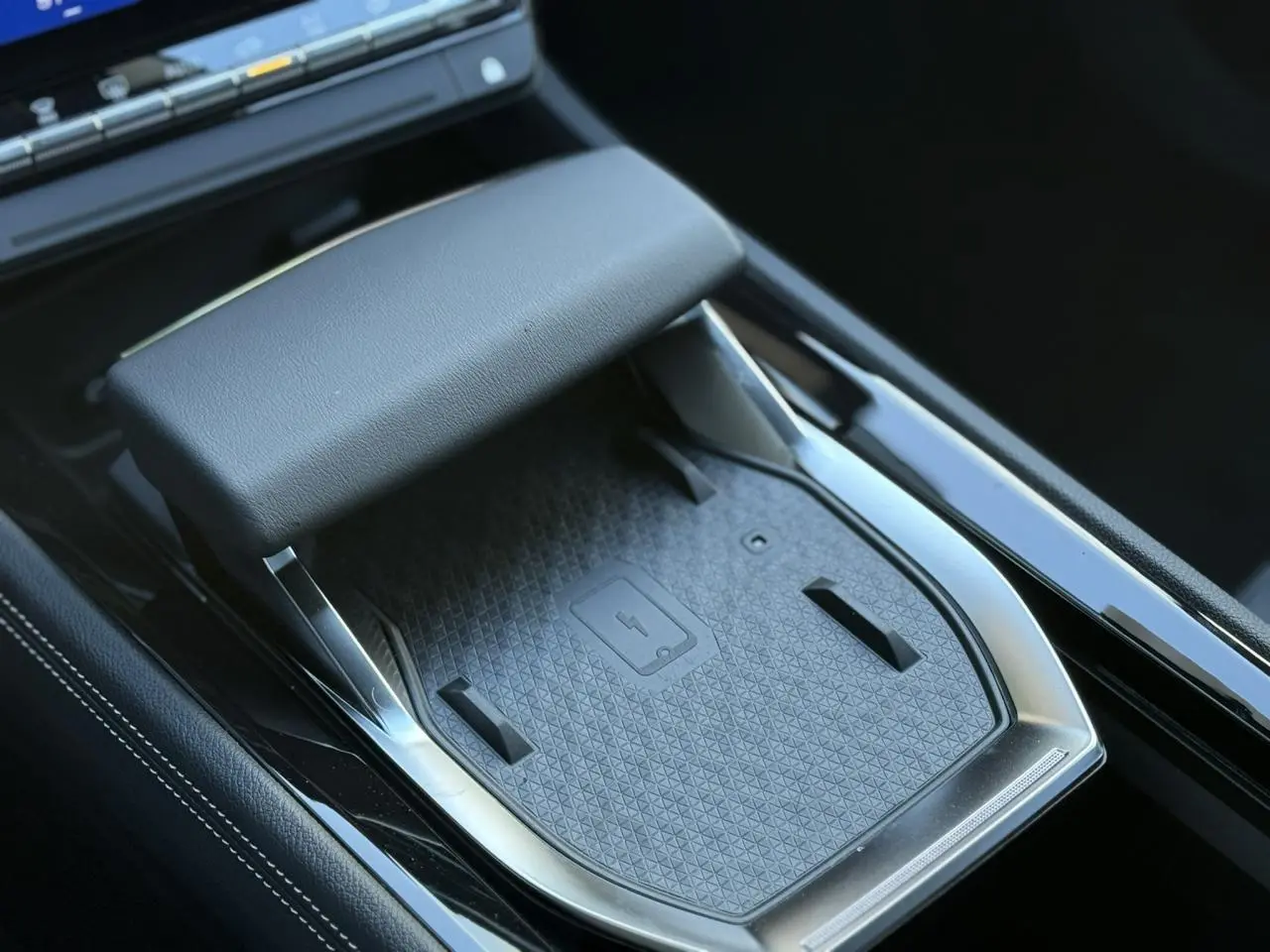 Détail de la console centrale noire du Renault Espace VI hybride avec chargeur smartphone à induction et accoudoir.