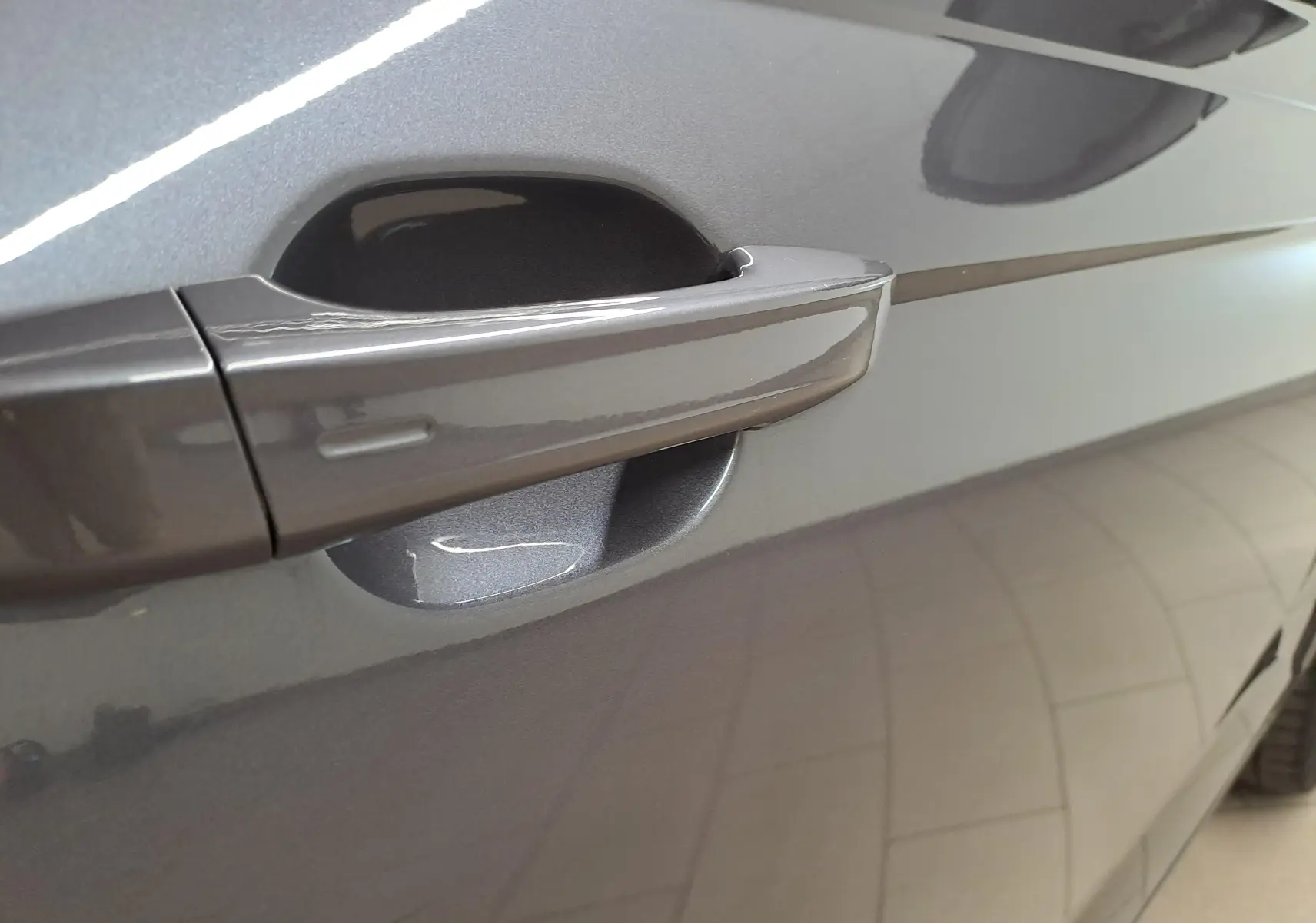 Poignée de porte côté gauche en gros plan sur Volkswagen Taigo gris cendré métallisé avec reflet de lumière.