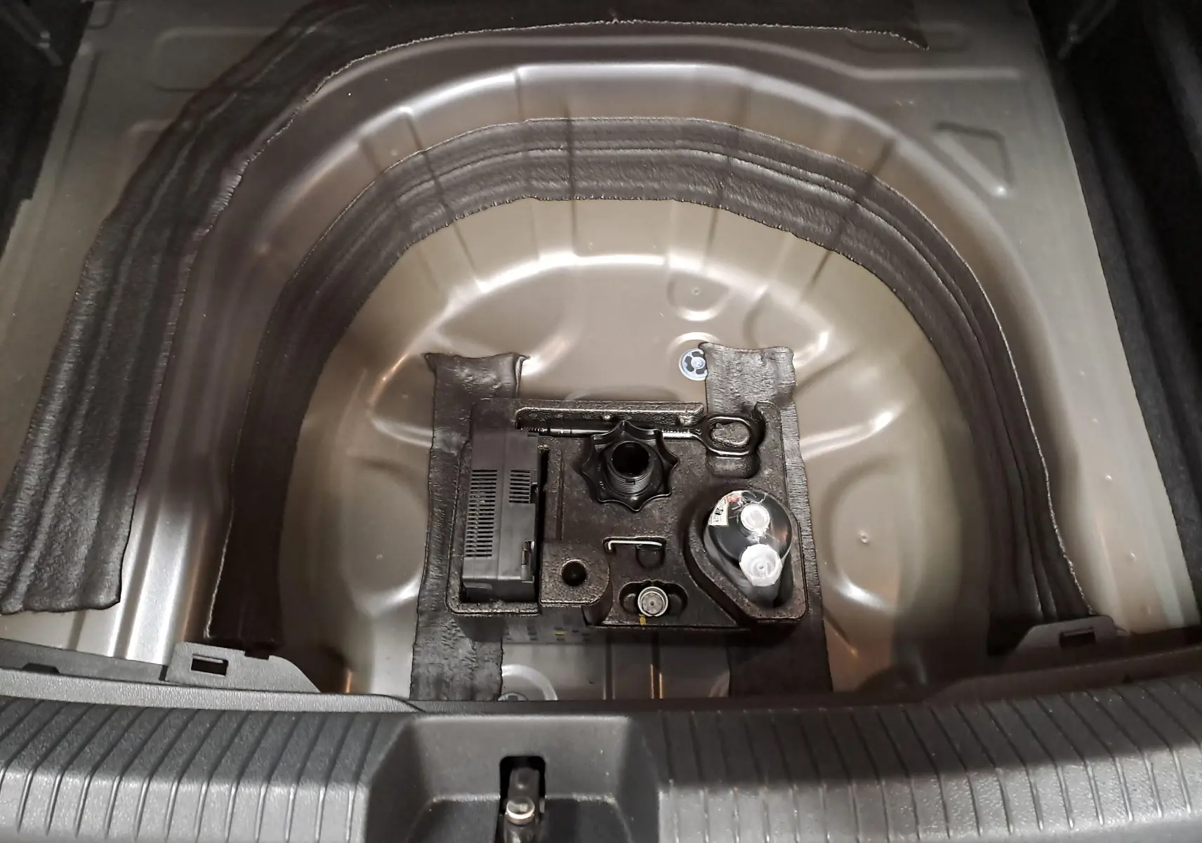 Vue plongeante sur le coffre ouvert du Volkswagen Taigo gris cendré, montrant le rangement sous le plancher sans roue de secours.