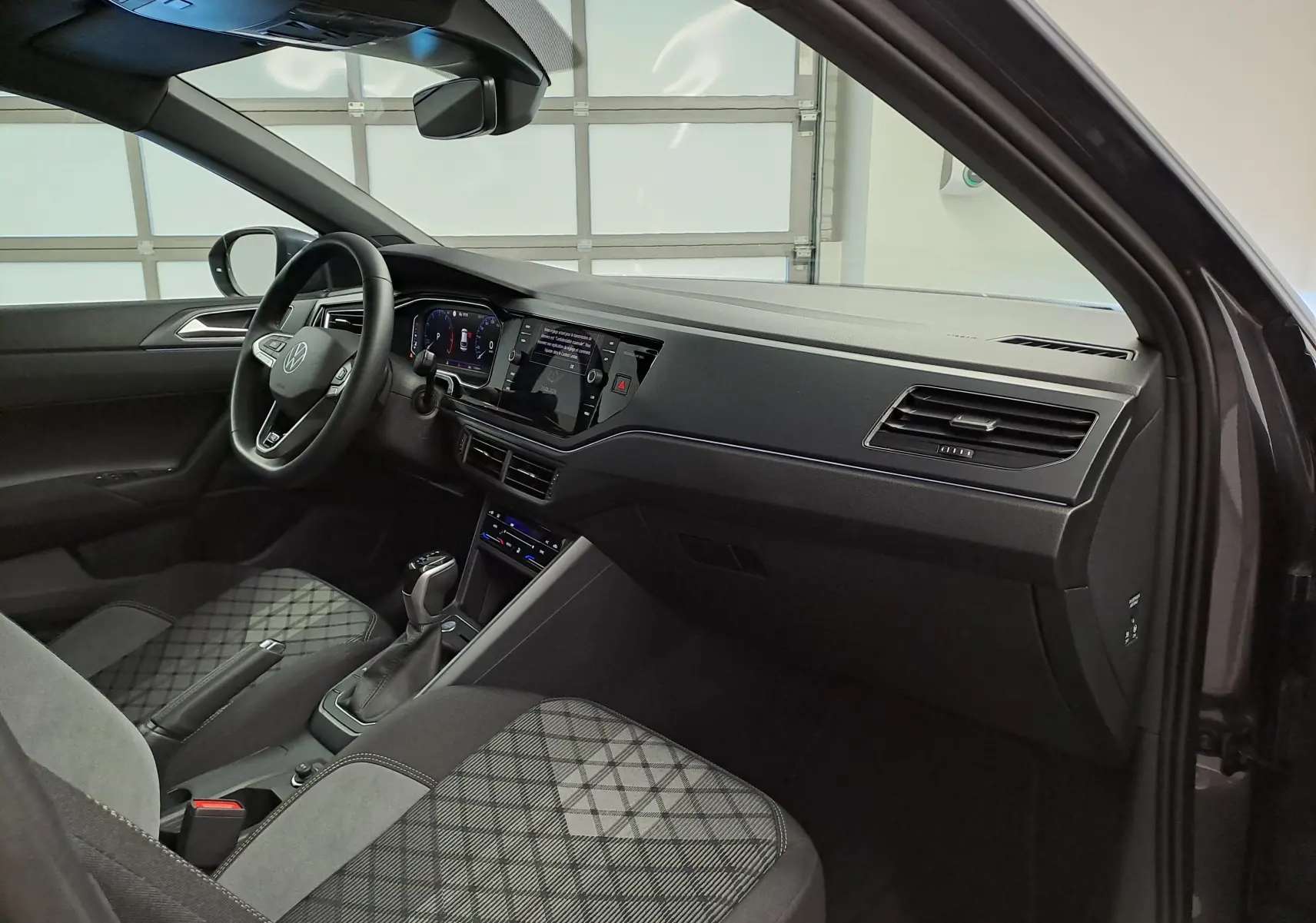 Vue intérieure côté conducteur du Volkswagen Taigo 1.0 TSI 116 DSG7 R-Line Edition avec sièges tissu gris à motifs.