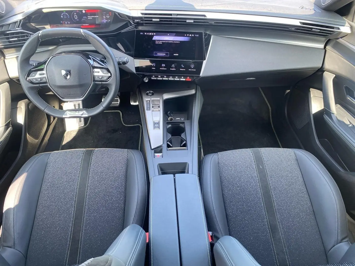 Intérieur Peugeot 308 1.2 hybrid 145 GT 2025, vue avant centrée sur tableau de bord, volant compact et sièges tissu cuir gris.