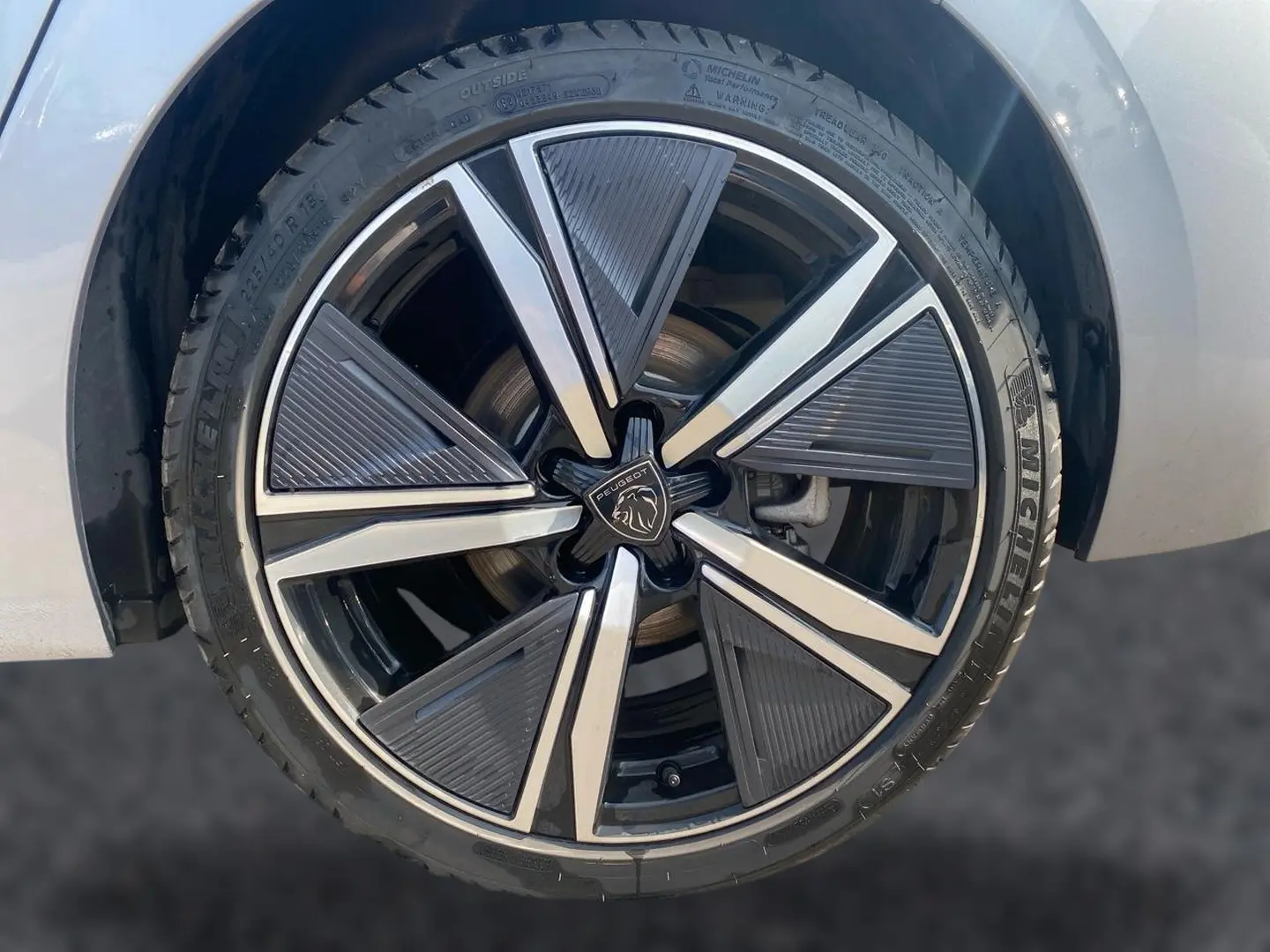 Gros plan sur la jante alu noire et argentée d’une Peugeot 308 gris clair, mettant en valeur le logo central Peugeot.