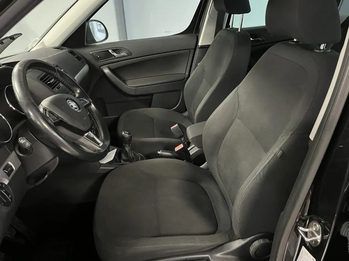 Vue intérieure côté conducteur du Skoda Yeti 2015 avec sièges tissu noirs et volant multifonctions cuir.