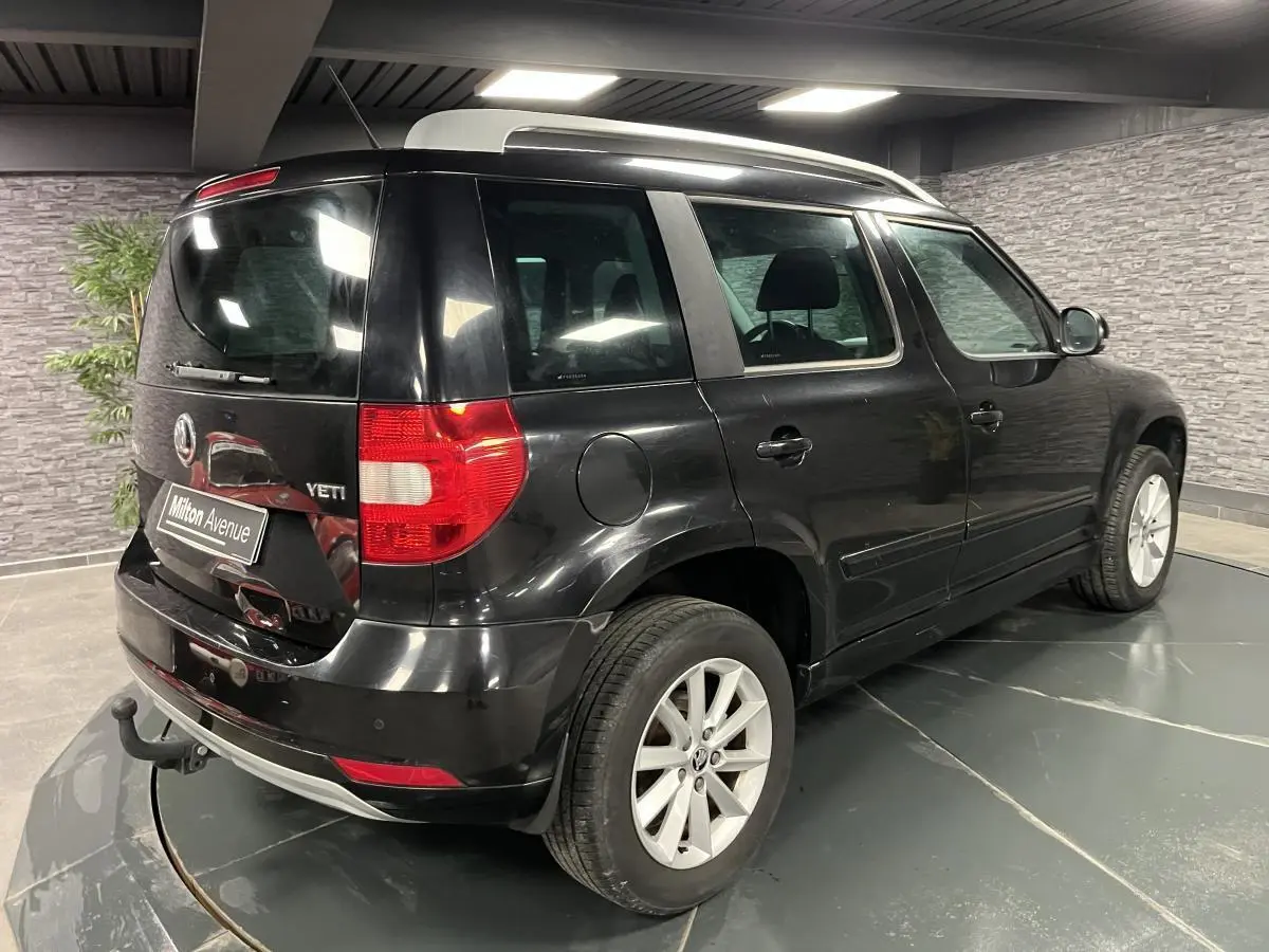 Vue 3/4 arrière droite d'un Skoda Yeti noir avec attelage et jantes alliage 16 pouces dans un showroom.