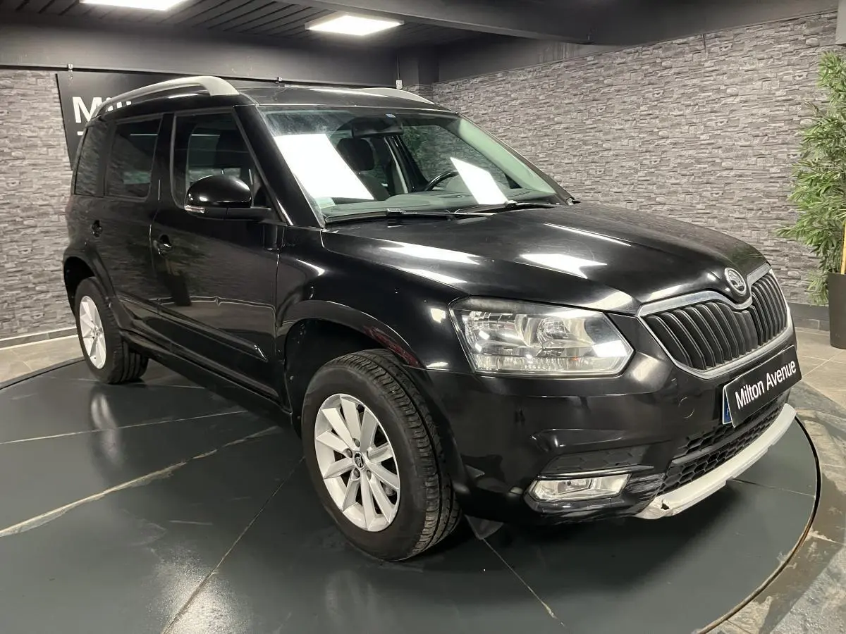 Vue 3/4 avant droite d'un Skoda Yeti noir avec jantes alliage et barres de toit argentées en intérieur showroom.