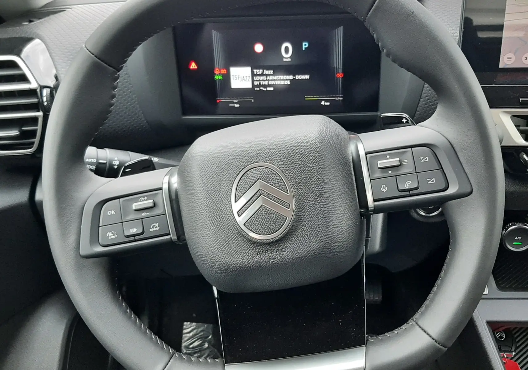 Vue rapprochée du volant multifonction noir du Citroën C4 1.2 Hybride 145ch avec tableau de bord numérique allumé.