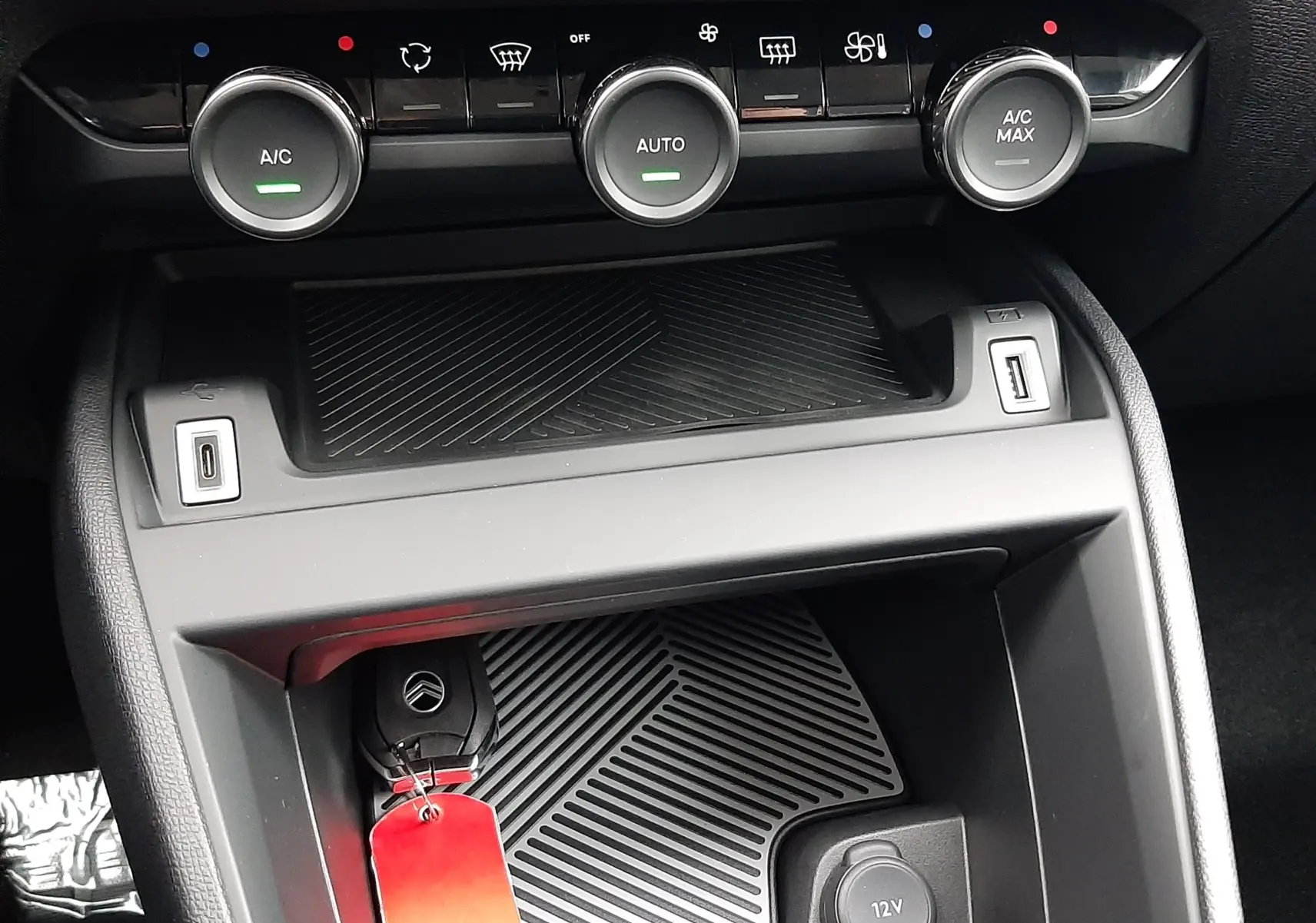 Gros plan sur la console centrale de la Citroën C4 hybride 2025, avec commandes climatisation et clé de voiture.