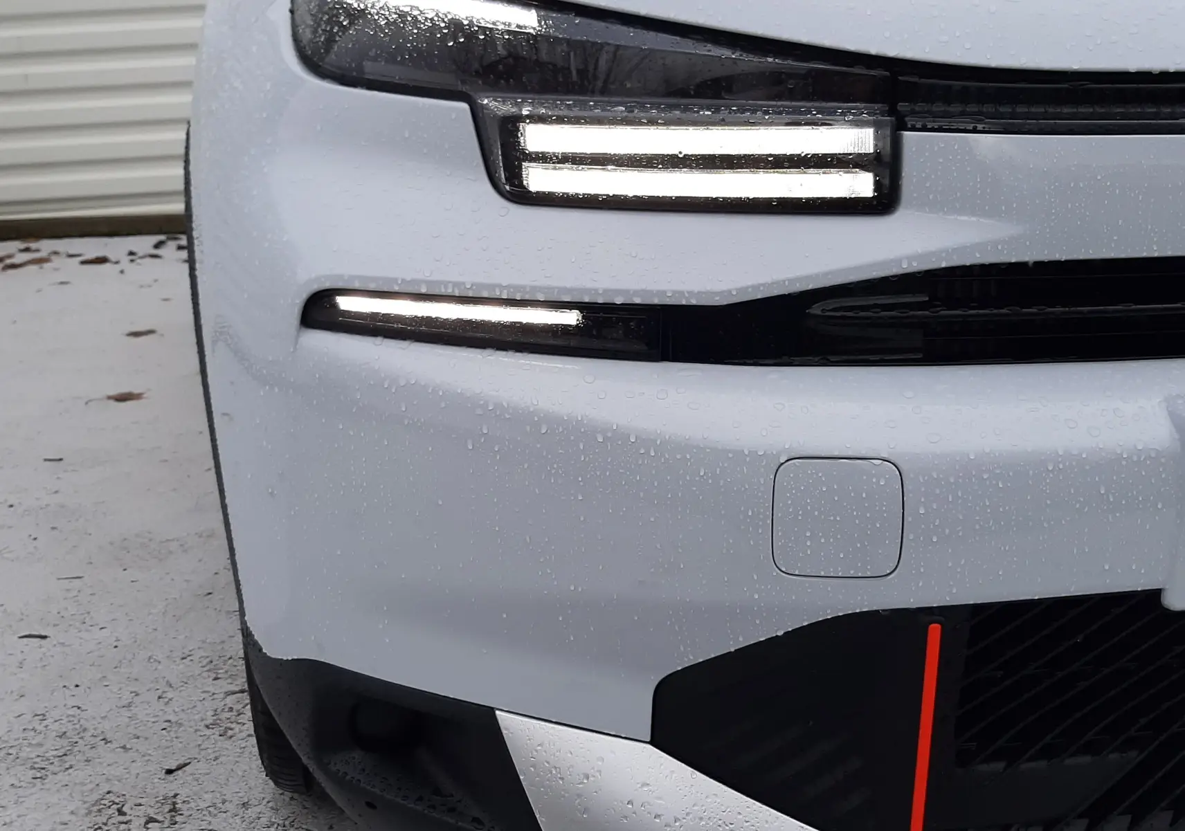 Gros plan sur l'avant gauche blanc Okenite avec toit noir Perla de la Citroën C4 hybride 2025, feux LED allumés.