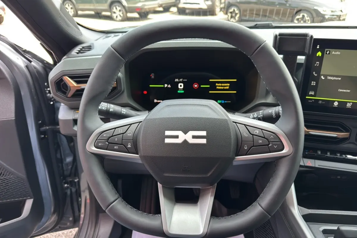Vue intérieure centrée sur le volant cuir noir du Dacia Bigster Hybrid 155 Extreme Plus avec tableau de bord digital allumé.