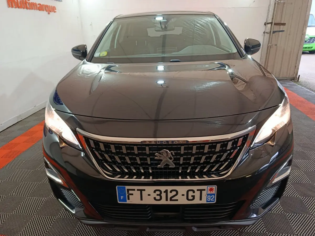Vue frontale d'un Peugeot 3008 noir avec calandre chromée et phares allumés en intérieur.