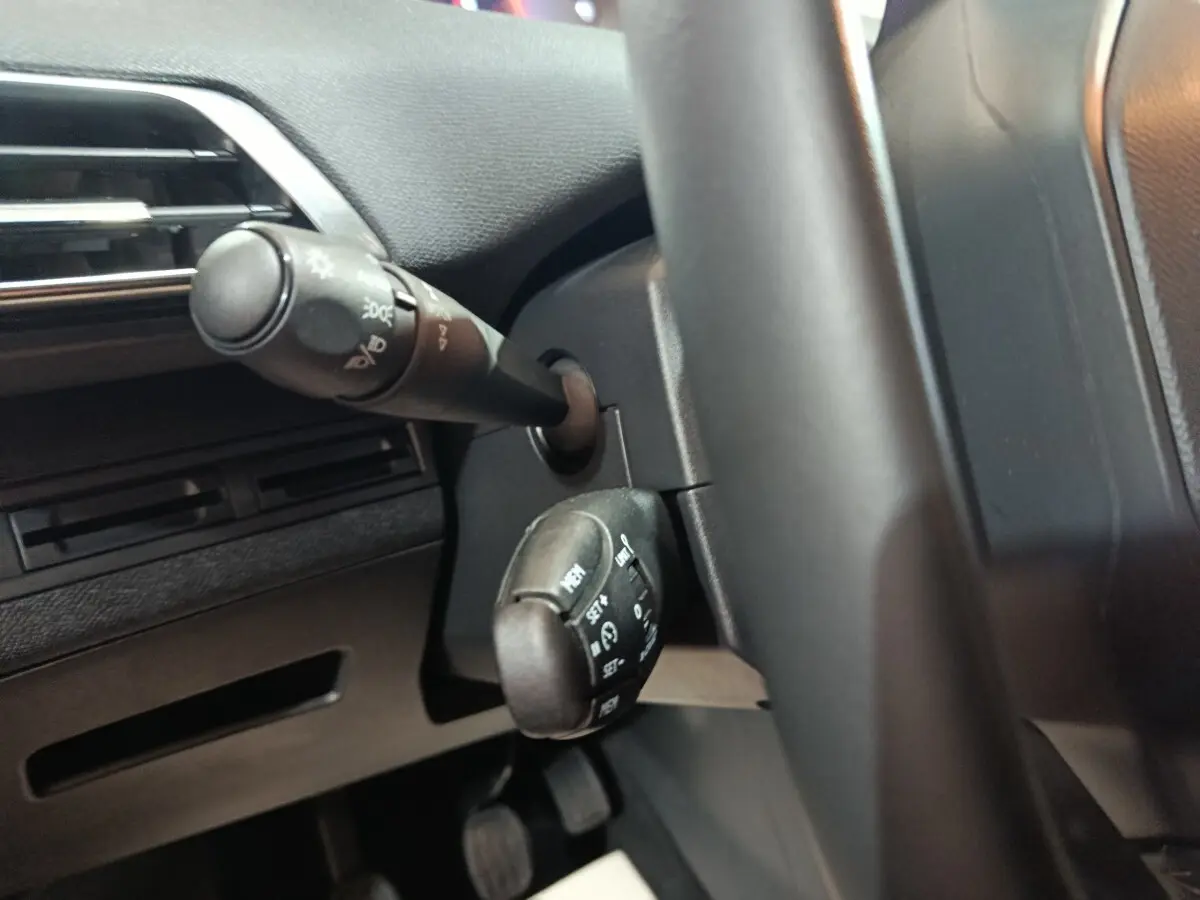 Gros plan sur les commandes au volant noir du Peugeot 3008 2020 BlueHDi, avec levier de clignotants et régulateur de vitesse.