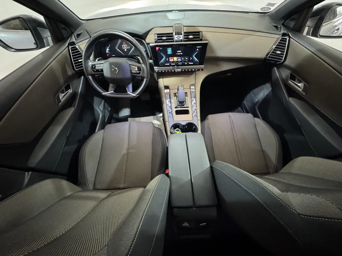 Vue intérieure avant du DS7 Crossback E-TENSE 225 Bastille+ montrant le tableau de bord noir avec écran tactile central et volant cuir.