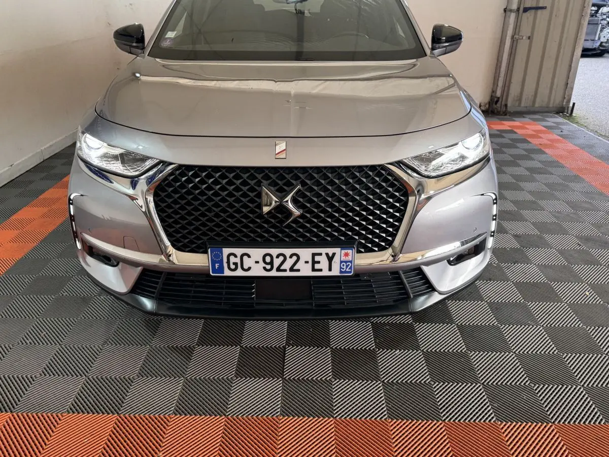 Vue avant d'un DS7 Crossback gris foncé avec calandre noire à motif losange et phares LED allumés.