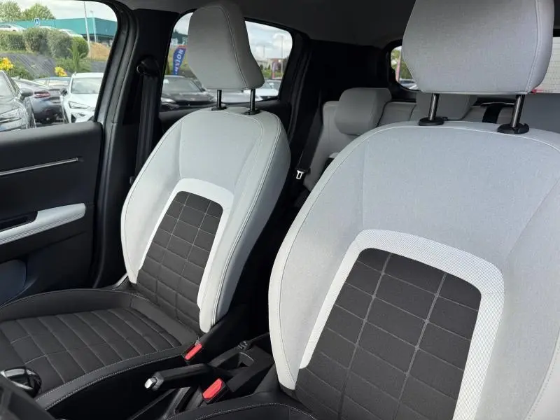Vue intérieure des sièges avant en tissu clair et noir de la Citroën C3 1.2 Turbo 100ch MAX, avec accoudoirs et ceintures visibles.