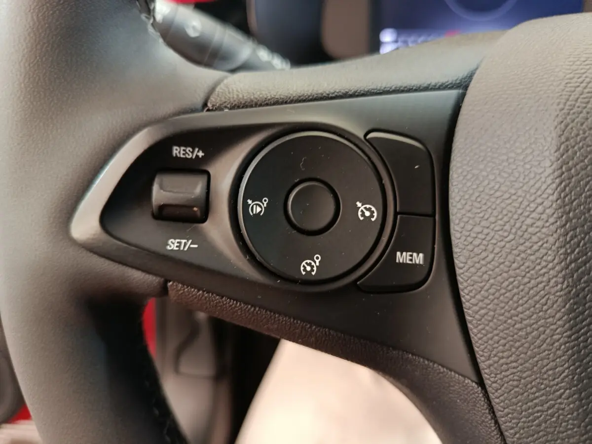 Gros plan sur les commandes de régulateur de vitesse au volant cuir noir de l’Opel Corsa rouge 2023.