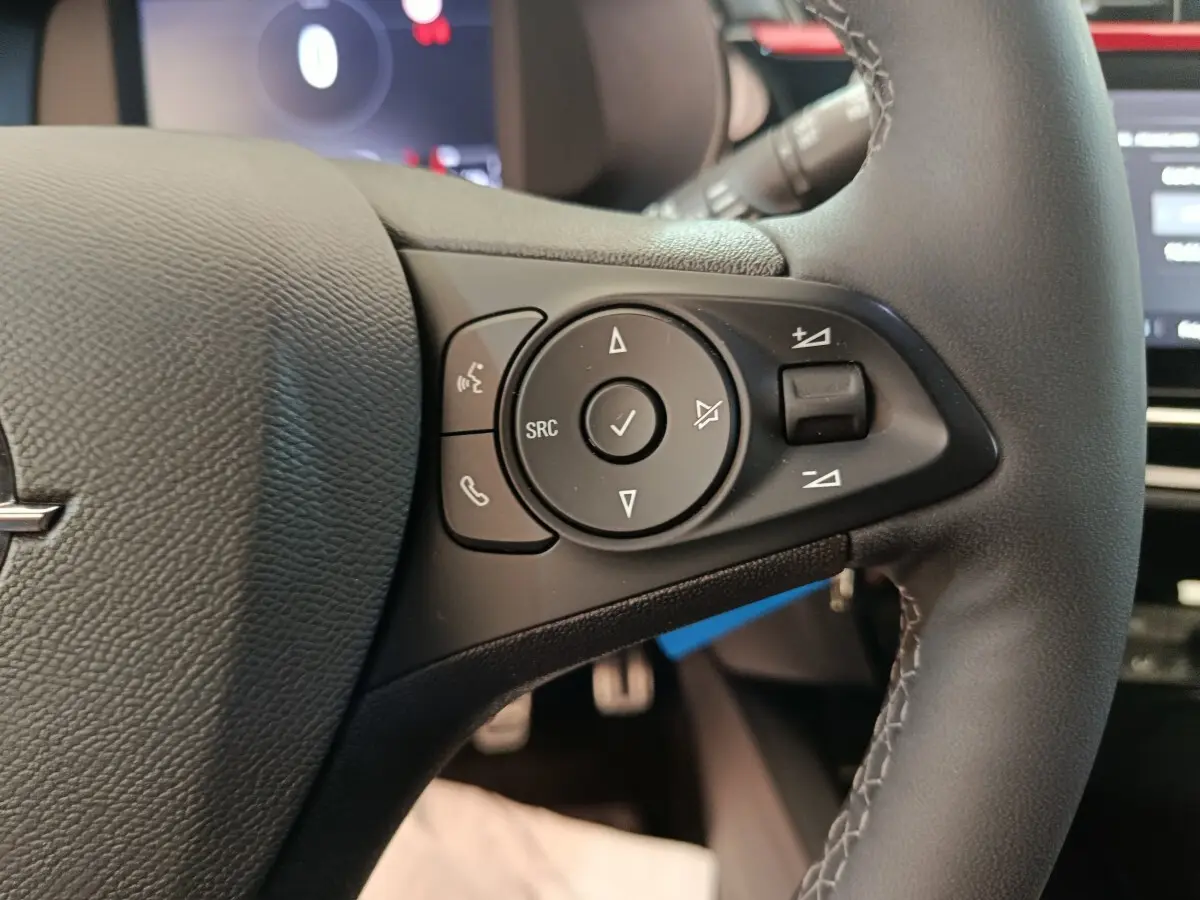 Gros plan sur les commandes gauche du volant cuir noir de l’Opel Corsa rouge 2023, avec boutons multifonctions.