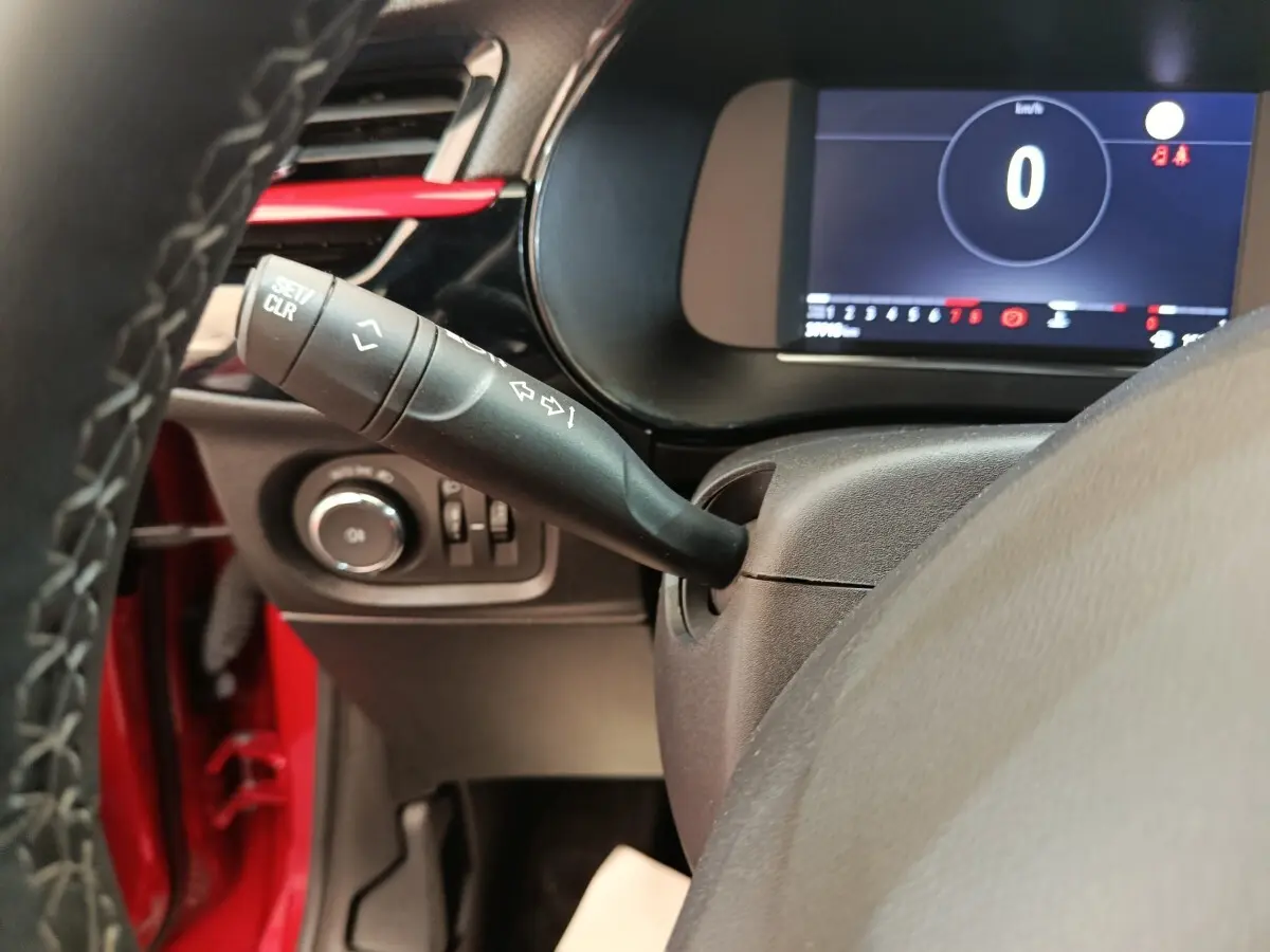 Gros plan sur la manette de clignotant et le combiné d'instruments numérique d'une Opel Corsa rouge, vue côté conducteur.