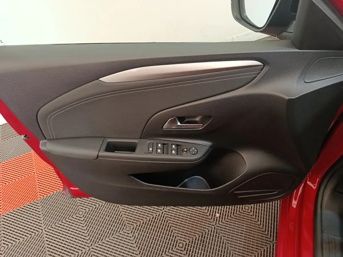 Vue intérieure côté gauche de la porte avant rouge d'une Opel Corsa 1.2 Turbo avec commandes électriques et garniture noire.