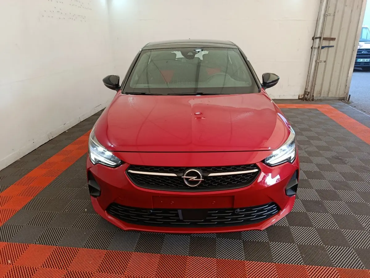 Vue frontale d'une Opel Corsa rouge 2023 avec calandre noire et phares LED allumés dans un garage.