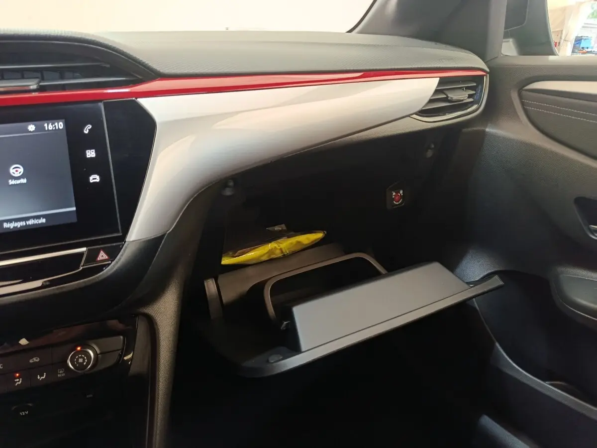 Intérieur de l’Opel Corsa rouge 2023, vue côté passager sur la boîte à gants ouverte et tableau de bord avec écran tactile.