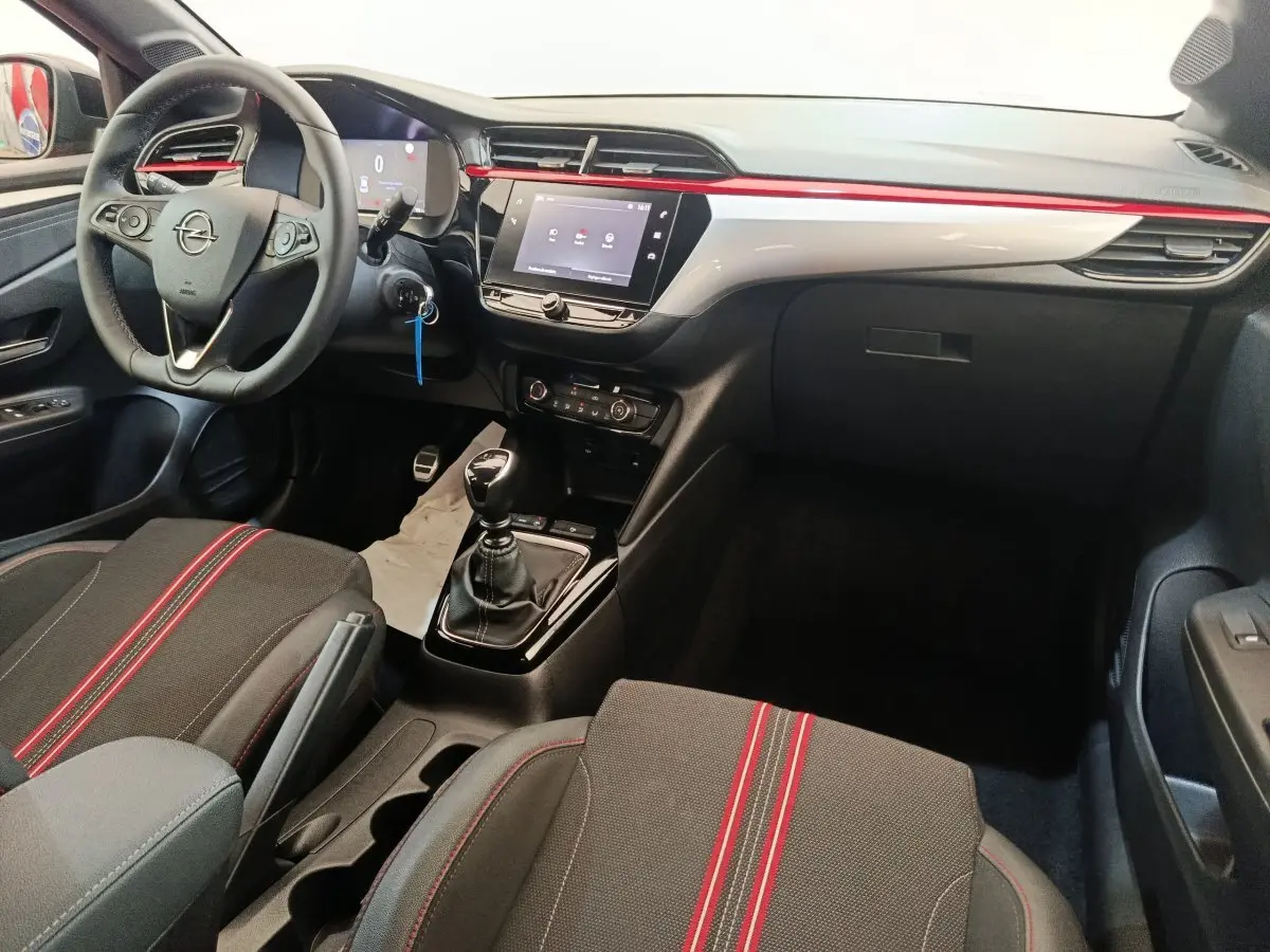 Vue intérieure côté conducteur de l’Opel Corsa 1.2 Turbo 2023, volant cuir, console centrale avec écran tactile et surpiqûres rouges.