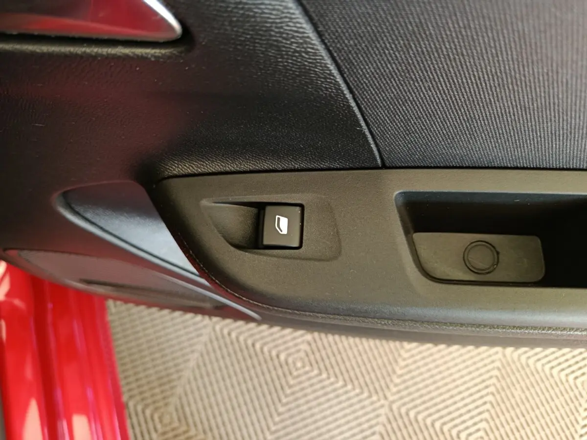 Gros plan sur la commande de lève-vitre côté conducteur d’une Opel Corsa rouge, intérieur noir.